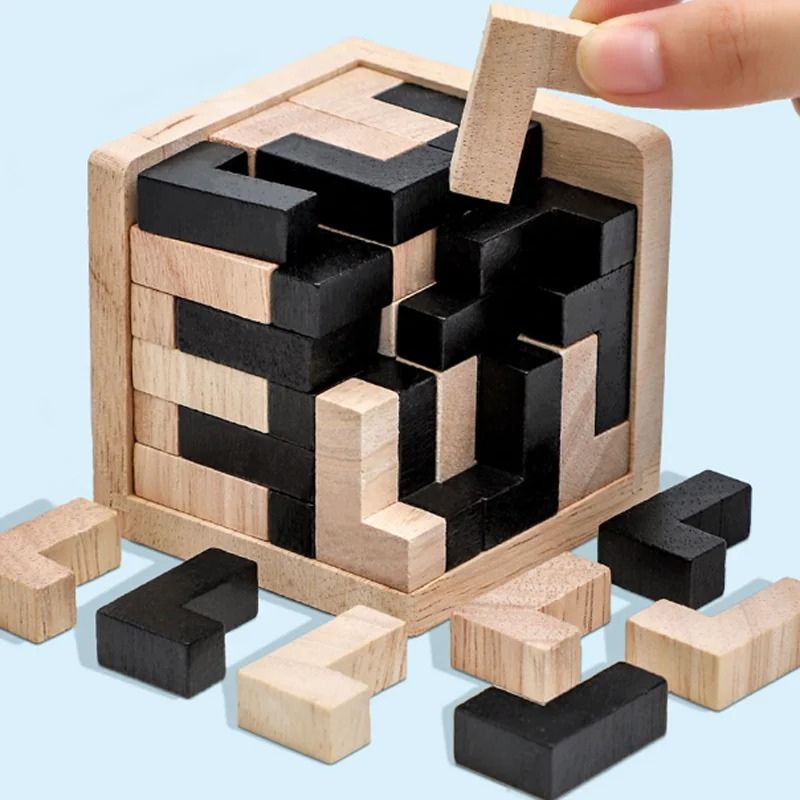 Gros plan main adulte qui pose un bloc bois naturel sur le puzzle cube 3D naturel noir fond bleu - qualité matériau jouet enfant - Atelier Puzzle